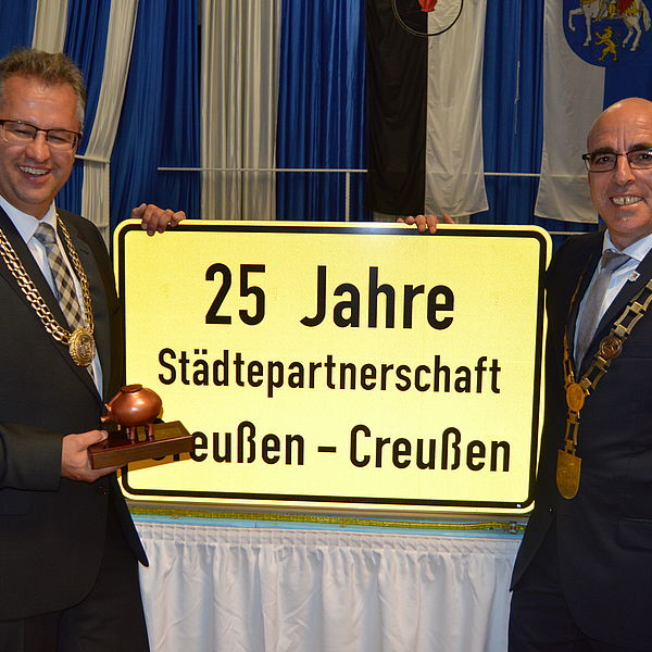 Die beiden Bürgermeister Martin Dannhäußer und René Hartnauer halten ein Schild mit der Aufschrift "25 Jahre Städtepartnerschaft Greußen - Creußen"